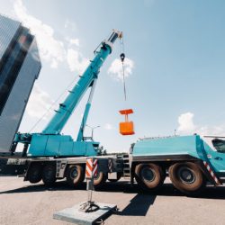 A large blue truck crane stands ready for operation on a site near a large modern building. The largest truck crane with a yellow cradle for solving complex tasks.